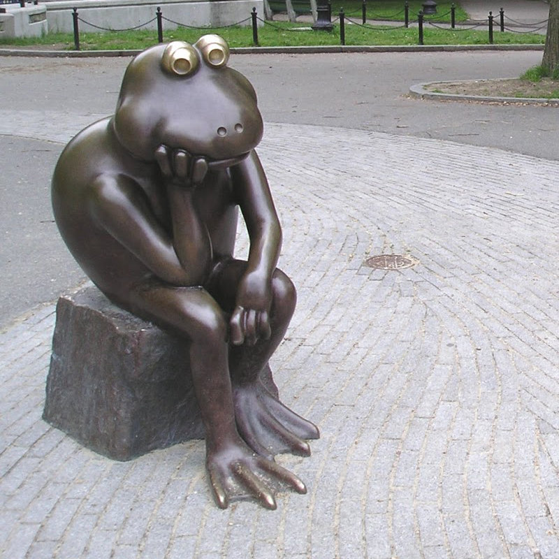 A sculpture of a humpbacked frog ponders in a park garden