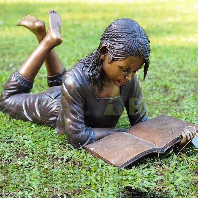 The little girl is reading a book on the lawn