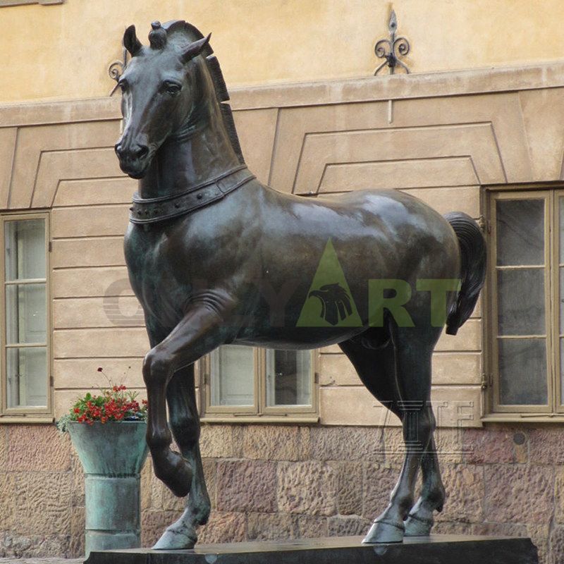 A statue of a horse in front of a large manor