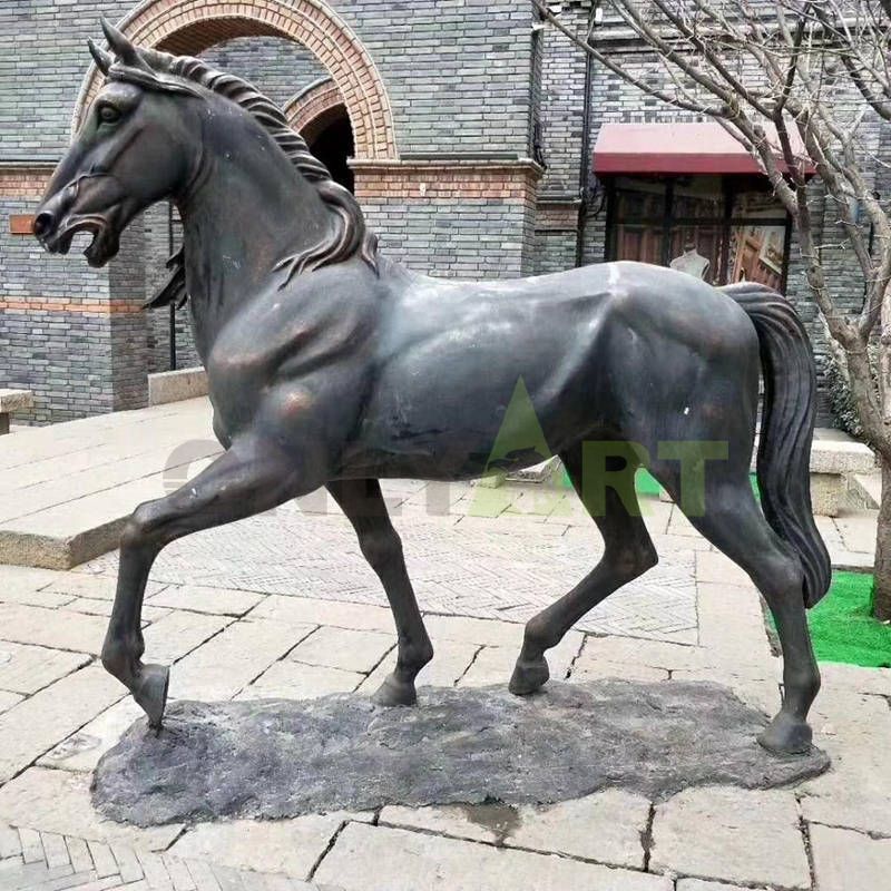 A statue of a horse in front of a large manor