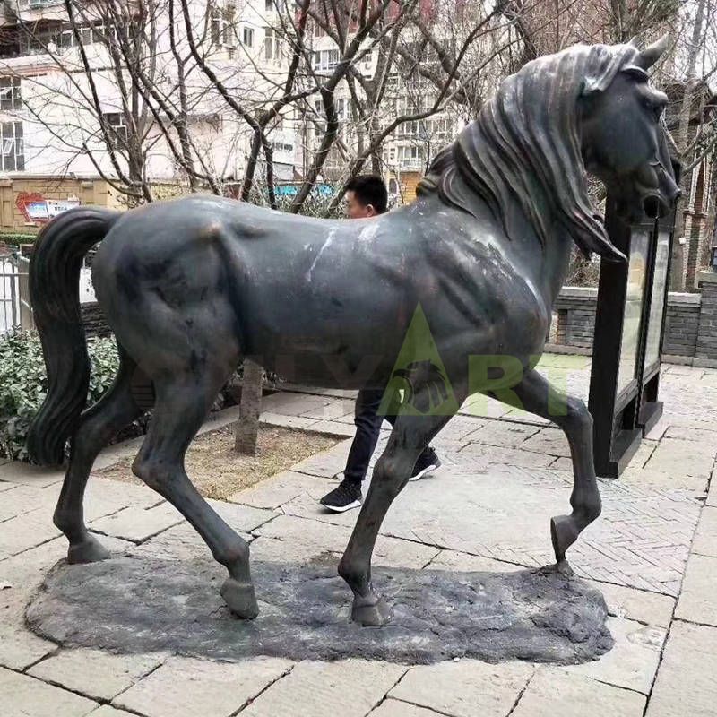 A statue of a horse in front of a large manor