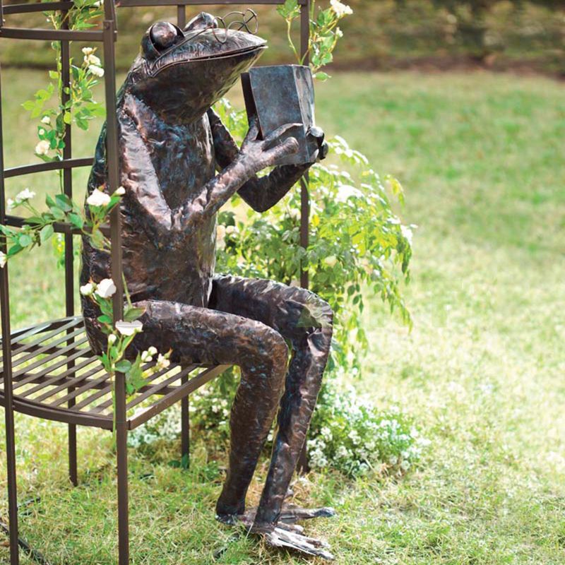 A sculpture of a frog sitting on a wicker chair holding a book