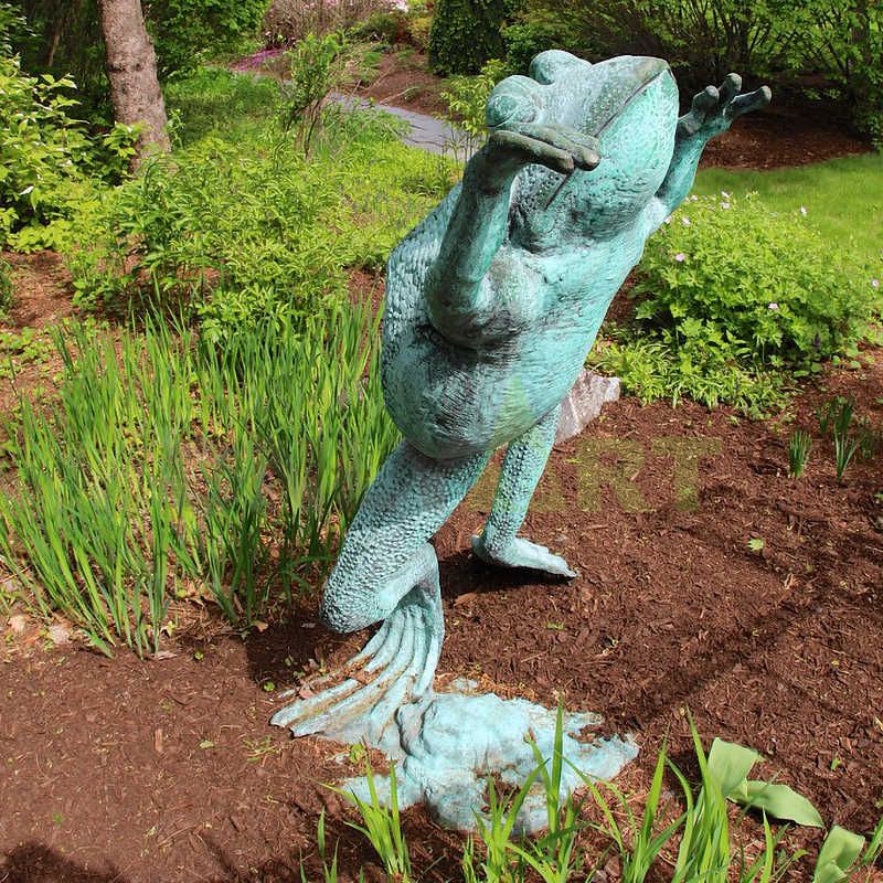 A sculpture of a frog sitting on a wicker chair holding a book